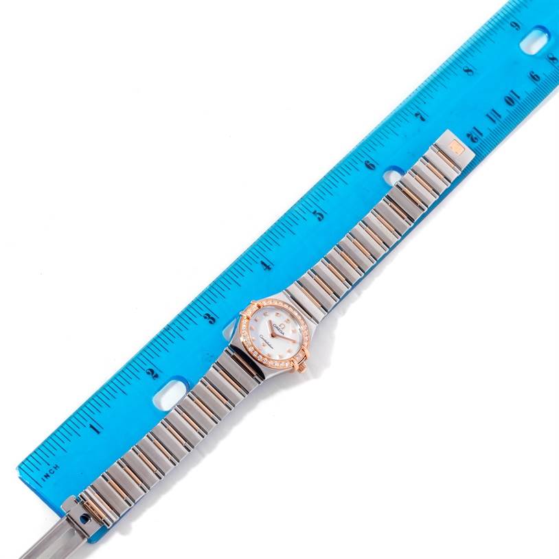 The image shows an Omega 1368.71.00 Women
s Steel and Gold (two tone) Mother of Pearl Dial 1368.71.00 Women
s Steel and Gold (two tone) Mother of Pearl Dial Constellation My Choice Mini Diamond Watch 1368.71.00 laid flat and measured with a blue ruler.