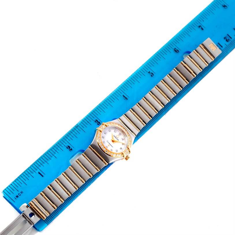 The Omega 1267.75.00 Women
s Steel and Gold (two tone) Mother of Pearl Dial 1267.75.00 Women
s Steel and Gold (two tone) Mother of Pearl Dial Constellation My Choice Steel Gold Diamond Watch 1267.75.00 is shown laying flat next to a blue ruler.