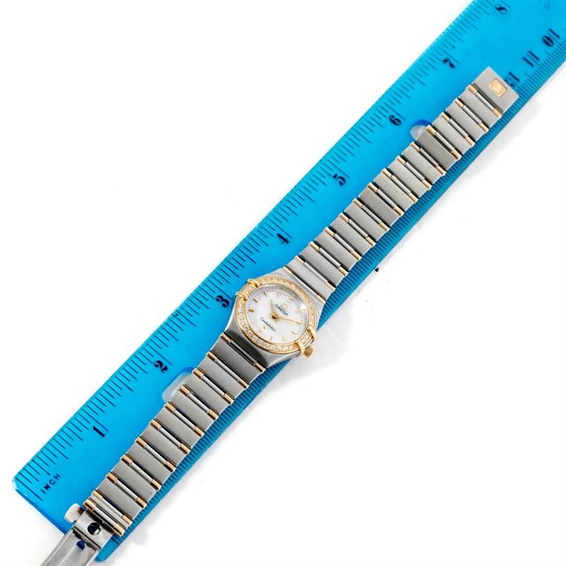 The Omega 56945066 Women
s Steel and Gold (two tone) Mother of Pearl Dial 56945066 Women
s Steel and Gold (two tone) Mother of Pearl Dial Constellation Mini Steel and Gold Diamond Watch is shown lying flat against a blue ruler, displaying the full bracelet and face.