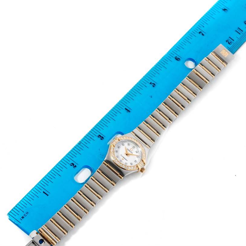 The Omega 1267.75.00 Women
s Steel and Gold (two tone) Mother of Pearl Dial 1267.75.00 Women
s Steel and Gold (two tone) Mother of Pearl Dial Constellation My Choice 1267.75.00 watch is shown flat with its steel and gold band alongside a blue ruler.