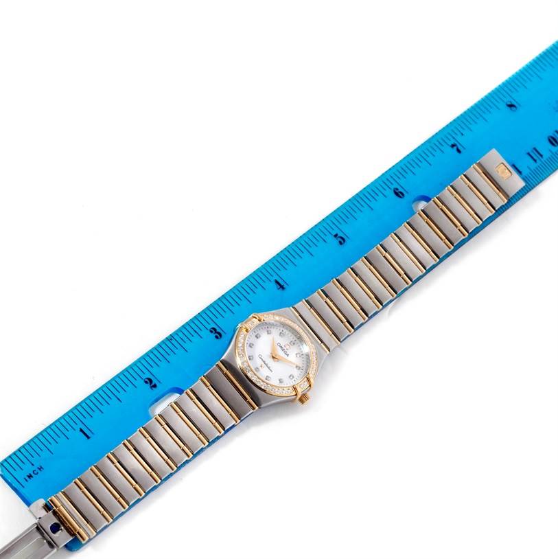 The image shows an Omega 1277.75.00 Women
s Steel and Gold (two tone) Mother of Pearl Dial 1277.75.00 Women
s Steel and Gold (two tone) Mother of Pearl Dial Constellation My Choice Steel Gold Diamond Watch 1277.75.00 laid flat next to a blue ruler for measurement.