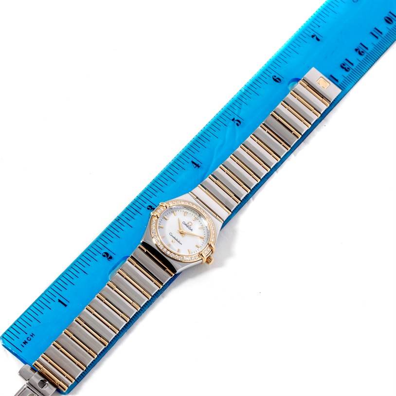The image shows the face and band of the Omega 1277.70.00 Women
s Steel and Gold (two tone) Mother of Pearl Dial 1277.70.00 Women
s Steel and Gold (two tone) Mother of Pearl Dial Constellation My Choice Steel Gold Diamond Watch 1277.70.00 with a blue ruler beside it.