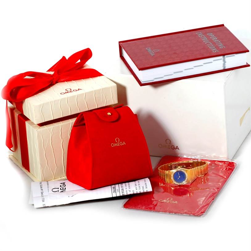 The image shows the Omega Women
s Blue Dial Women
s Blue Dial Constellation 18K Yellow Gold Diamond Lapis Dial Watch along with its packaging, manual, and accessories from a front angle.