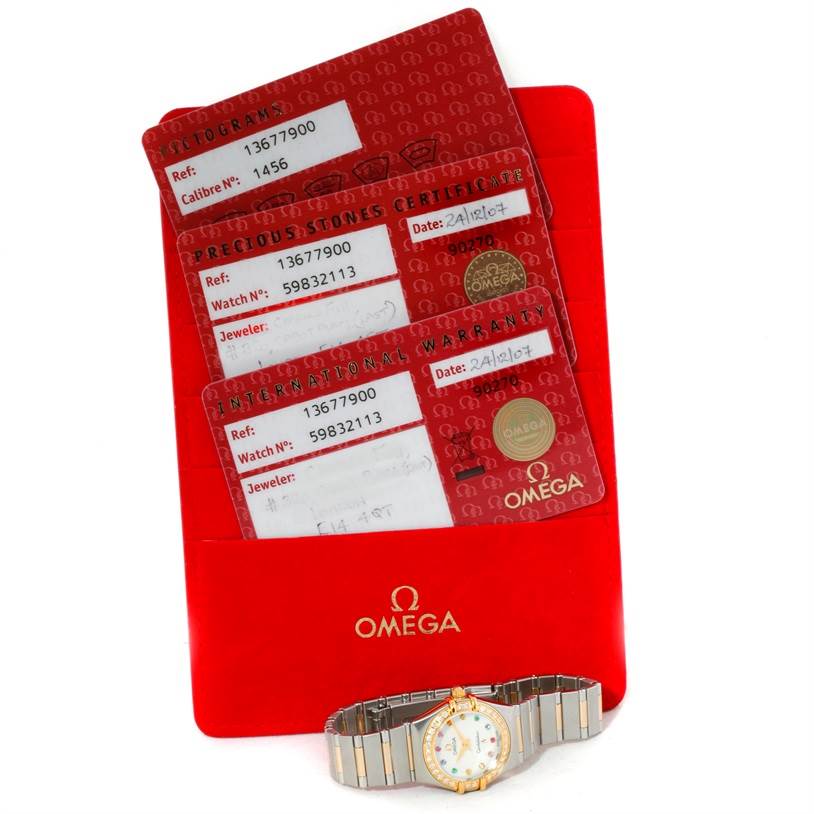 The image shows Omega 1367.79.00 Women
s Steel and Gold (two tone) Mother of Pearl Dial 1367.79.00 Women
s Steel and Gold (two tone) Mother of Pearl Dial Constellation Iris Steel Yellow Gold Multi Stone Watch 1367.79.00 with its warranty cards and holder, viewed from above.
