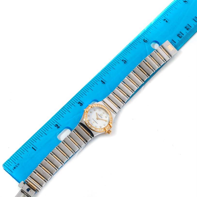 The Omega 1365.71.00 Women
s Steel and Gold (two tone) Mother of Pearl Dial 1365.71.00 Women
s Steel and Gold (two tone) Mother of Pearl Dial Constellation Mini Steel Yellow Gold Diamond Watch 1365.71.00 is shown from a top-down angle with a blue ruler for scale.