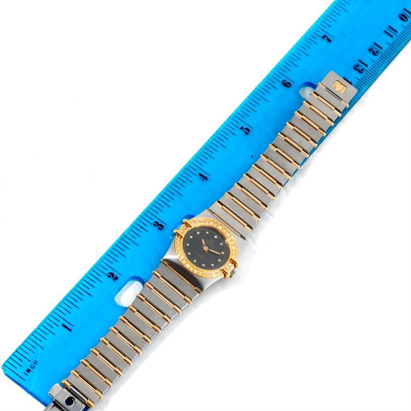 The image shows an Omega Women's Steel and Gold (two tone) Black Dial Women's Steel and Gold (two tone) Black Dial Constellation My Choice Mini Steel Gold Diamond Watch placed next to a ruler, displaying the entire band and face.