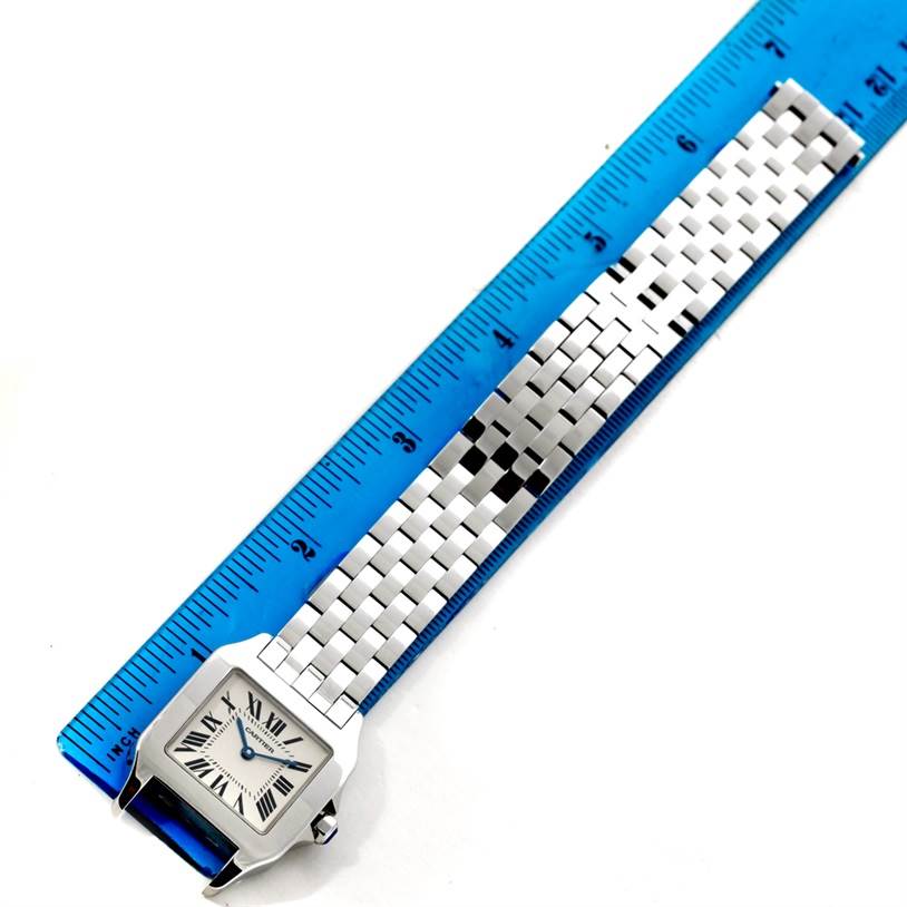 The Cartier Santos Demoiselle W25065Z5 Women
s Stainless Steel Silver Dial W25065Z5 Women
s Stainless Steel Silver Dial watch is shown from a top-down angle, highlighting its face and metal bracelet alongside a ruler.