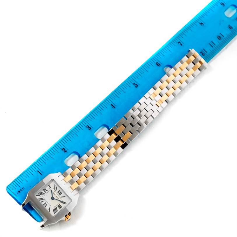 The image shows a Cartier Santos Demoiselle W25067Z6 Women's Steel and Gold (two tone) Silver Dial W25067Z6 Women's Steel and Gold (two tone) Silver Dial watch laying flat next to a blue ruler, highlighting its band and face.