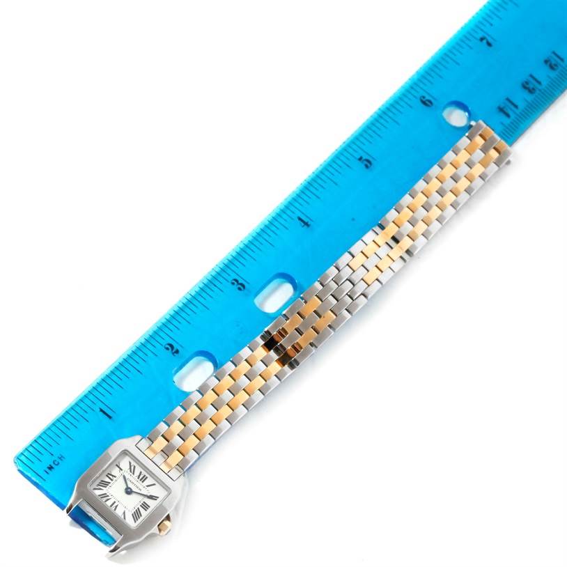 The image shows the front view of a Cartier Santos Demoiselle W25066Z6 Women's Steel and Gold (two tone) Silver Dial W25066Z6 Women's Steel and Gold (two tone) Silver Dial watch with its bracelet measured against a blue ruler.