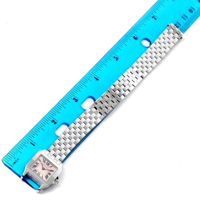 The image shows a Cartier Santos Demoiselle W25075Z5 Women
s Stainless Steel Mother of Pearl Dial W25075Z5 Women
s Stainless Steel Mother of Pearl Dial watch laid flat next to a blue ruler, displaying its face and metal bracelet.