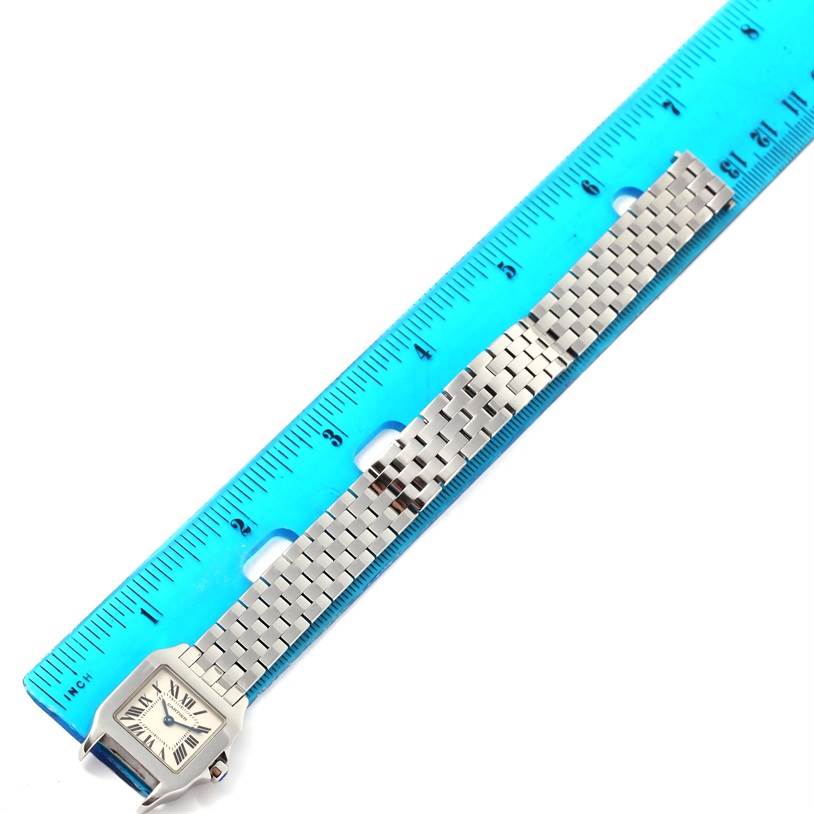 The image shows the Cartier Santos Demoiselle W25064Z5 Women's Stainless Steel Silver Dial W25064Z5 Women's Stainless Steel Silver Dial watch face and metal bracelet laid next to a blue ruler for measurement.
