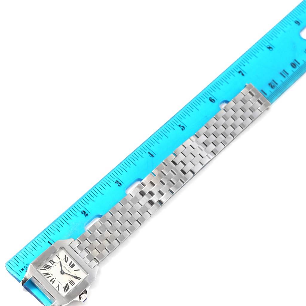 The image shows a Cartier Santos Demoiselle W25065Z5 Women's Stainless Steel Silver Dial W25065Z5 Women's Stainless Steel Silver Dial watch from a top-down angle, with its face and metal bracelet next to a blue ruler.