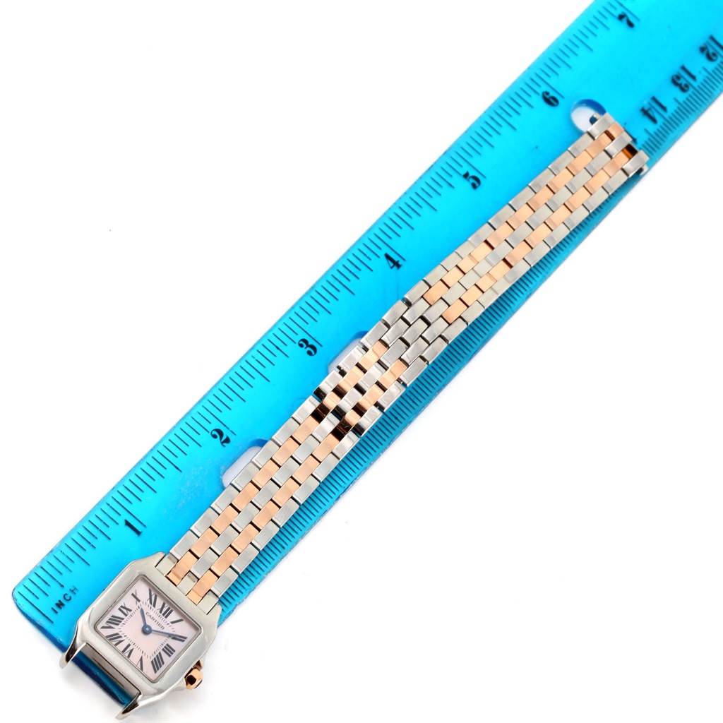 The image shows a top view of a Cartier Santos Demoiselle W25074Y9 Women's Steel and Gold (two tone) Mother of Pearl Dial W25074Y9 Women's Steel and Gold (two tone) Mother of Pearl Dial watch, highlighting its face and bracelet band next to a blue ruler.
