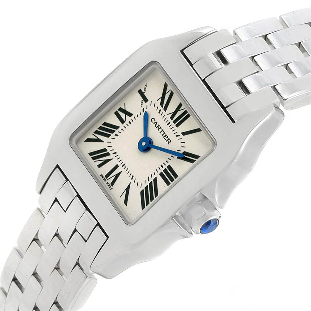 The image shows the Cartier Santos Demoiselle W25064Z5 Women's Stainless Steel Silver Dial W25064Z5 Women's Stainless Steel Silver Dial watch face, crown with blue gemstone, and part of the metal bracelet from an angled view.