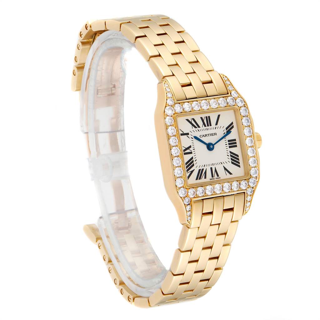 The Cartier Santos Demoiselle WF9002Y7 Women
s Yellow Gold Silver Dial WF9002Y7 Women
s Yellow Gold Silver Dial watch is shown at a three-quarter angle, highlighting its gold bracelet, diamond-studded bezel, and square face with Roman numerals.
