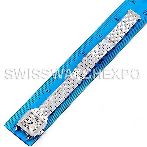 The Santos Demoiselle by Cartier is shown from a top-down angle, displaying its square face and entire metal bracelet beside a blue ruler.