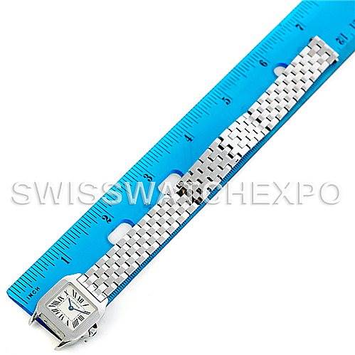 This image shows the Santos Demoiselle watch by Cartier laid flat against a ruler, highlighting its face and metal bracelet.