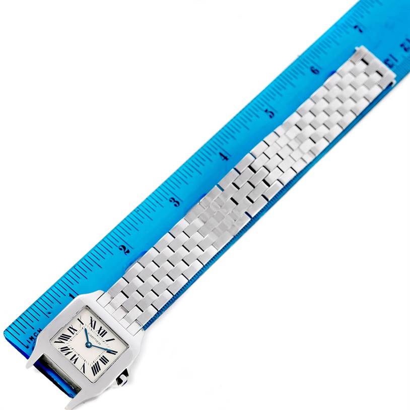 The image shows a Santos Demoiselle watch by Cartier, displayed next to a ruler, highlighting the face and metal bracelet.