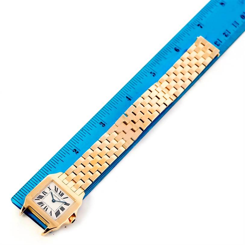 The Cartier Santos Demoiselle W25062X9 Women's Yellow Gold Silver Dial W25062X9 Women's Yellow Gold Silver Dial watch is shown from a top-down angle, featuring the watch face and bracelet alongside a blue ruler.