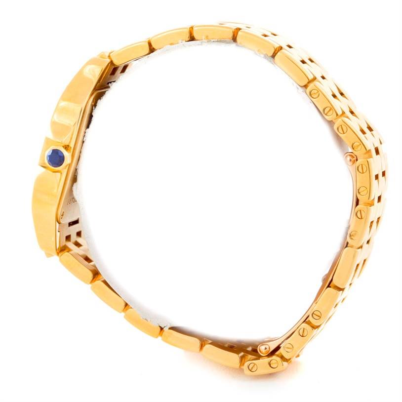 The image shows a side angle of the Cartier Santos Demoiselle W25062X9 Women
s Yellow Gold Silver Dial W25062X9 Women
s Yellow Gold Silver Dial watch, displaying its gold bracelet and crown with a blue gemstone.