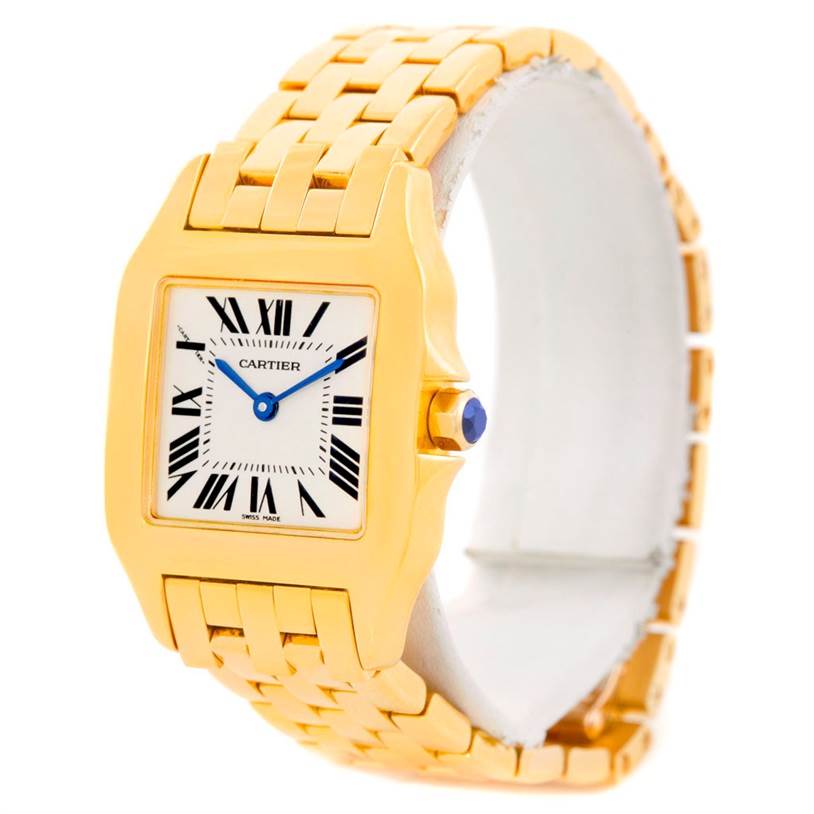 The image shows a Cartier Santos Demoiselle W25062X9 Women
s Yellow Gold Silver Dial W25062X9 Women
s Yellow Gold Silver Dial watch at an angled view, highlighting the gold bracelet, square face, crown with a blue gem, and Roman numeral markers.