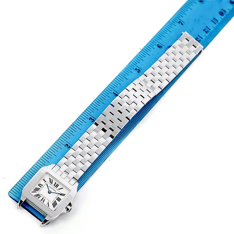 The image shows a Cartier Santos Demoiselle W25065Z5 Women
s Stainless Steel Silver Dial W25065Z5 Women
s Stainless Steel Silver Dial watch placed next to a blue ruler for scale, viewed from above.