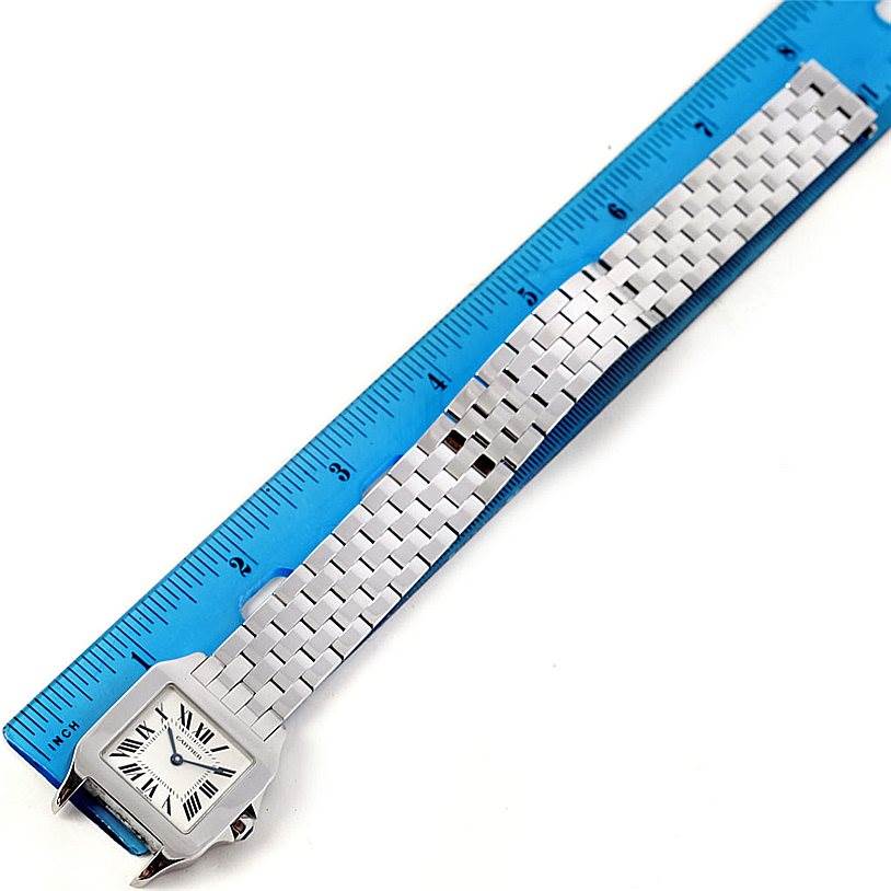 The image shows an overhead view of the Cartier Santos Demoiselle W25065Z5 Women
s Stainless Steel Silver Dial W25065Z5 Women
s Stainless Steel Silver Dial watch alongside a blue ruler, highlighting the bracelet and square face.