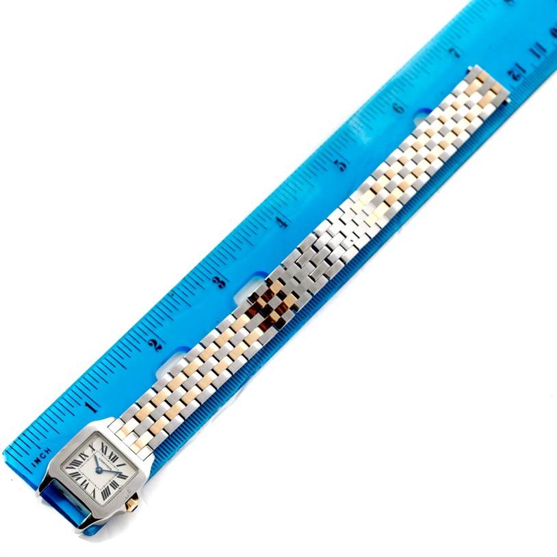 The image shows the Santos Demoiselle model by Cartier, including its face and entire band, next to a blue ruler for scale.