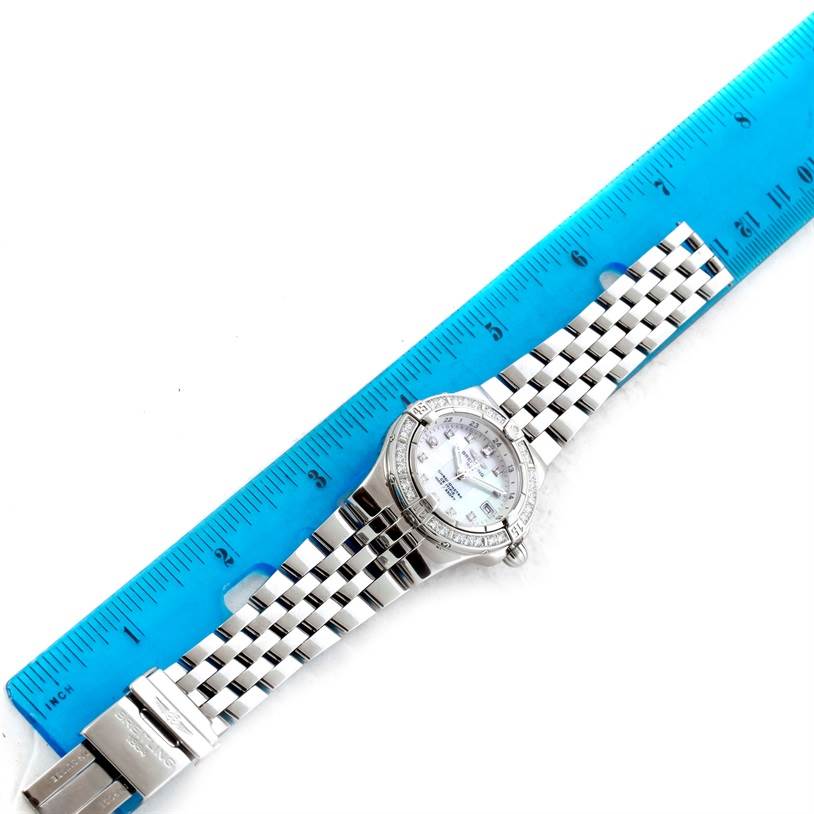 The Breitling A71340 Women's Stainless Steel Mother of Pearl Dial A71340 Women's Stainless Steel Mother of Pearl Dial Starliner Ladies Mother of Pearl Diamond Watch A71340 is shown flat with its bracelet extended next to a blue ruler.