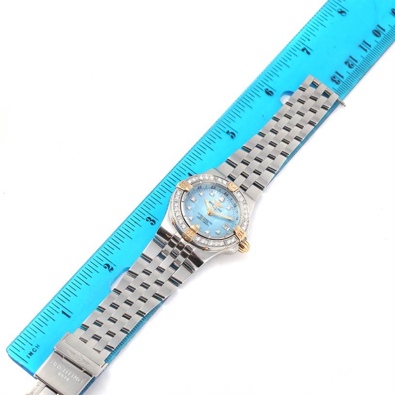 The Breitling WATCH Women's Steel and Gold (two tone) Mother of Pearl Dial WATCH Women's Steel and Gold (two tone) Mother of Pearl Dial Starliner Steel Yellow Gold Blue MOP Diamond Watch B71340 is shown from a top-down angle with the watch band extended next to a ruler.
