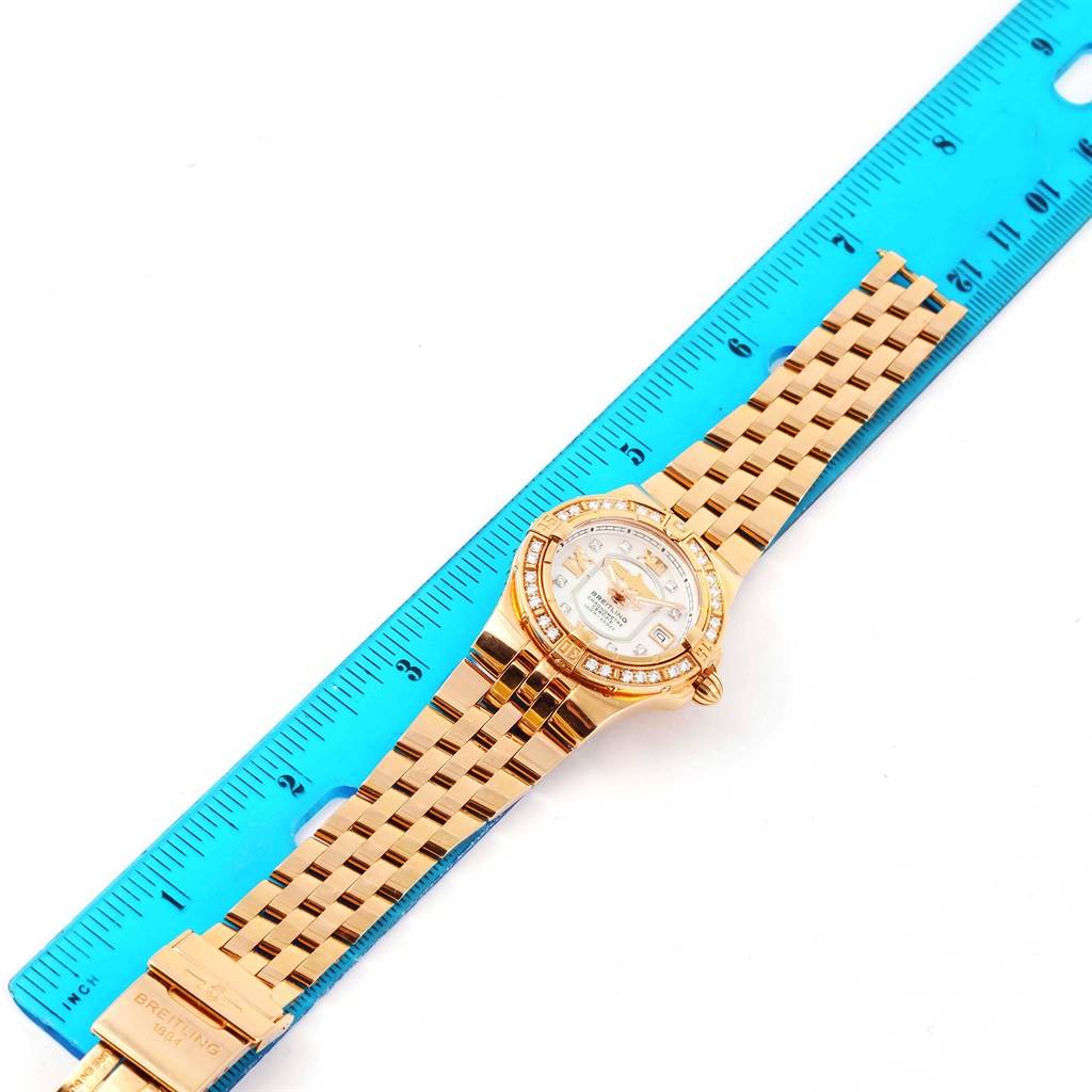 The Breitling H71340 Women's Rose Gold Mother of Pearl Dial H71340 Women's Rose Gold Mother of Pearl Dial Starliner 30 Mother of Pearl Diamond Watch H71340 is shown from a top-down angle, lying next to a blue ruler.