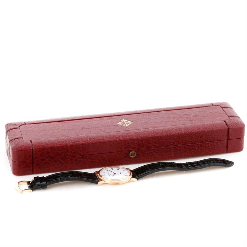 This image shows a Patek Philippe Calatrava 5119R Men's Rose Gold White Dial 5119R Men's Rose Gold White Dial watch, laid flat with a brown leather strap, next to its red box.