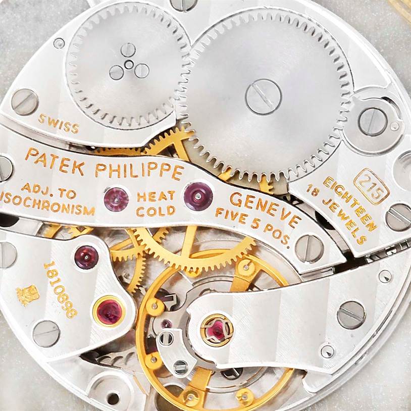 This close-up image shows the intricate movement parts of a Patek Philippe Calatrava 3919 Men's Yellow Gold White Dial 3919 Men's Yellow Gold White Dial watch, including gears and inscriptions.