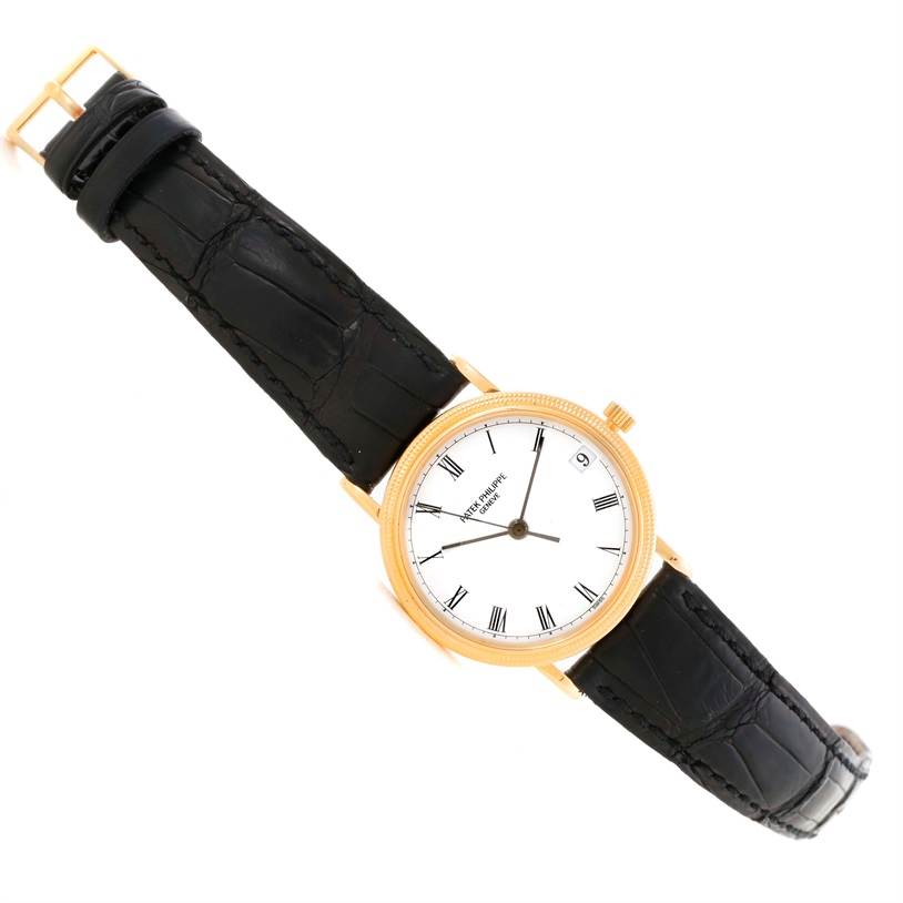 The image shows a top view of the Patek Philippe Calatrava 3802 Men's Yellow Gold White Dial 3802 Men's Yellow Gold White Dial watch featuring its black leather strap and gold casing.