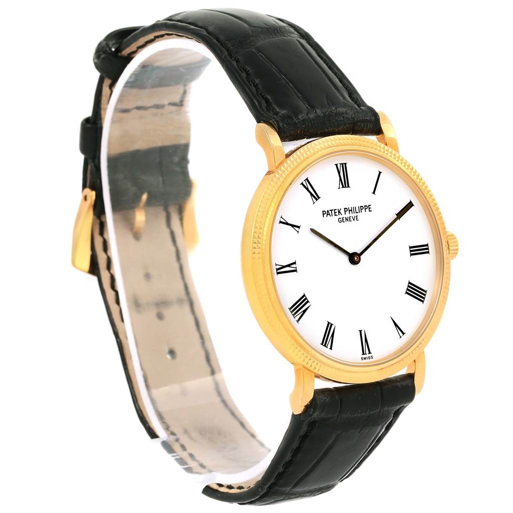 The Patek Philippe Calatrava 5120J Men's Yellow Gold White Dial 5120J Men's Yellow Gold White Dial watch is shown at a slight side angle, highlighting its gold case, white dial, Roman numerals, and black leather strap.