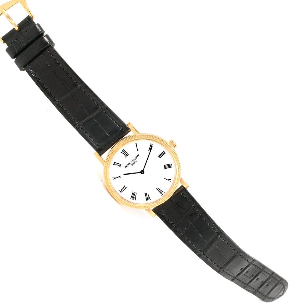 The image shows a top view of the Patek Philippe Calatrava 5120J Men's Yellow Gold White Dial 5120J Men's Yellow Gold White Dial watch, highlighting the entire watch, including its black leather strap and gold case.