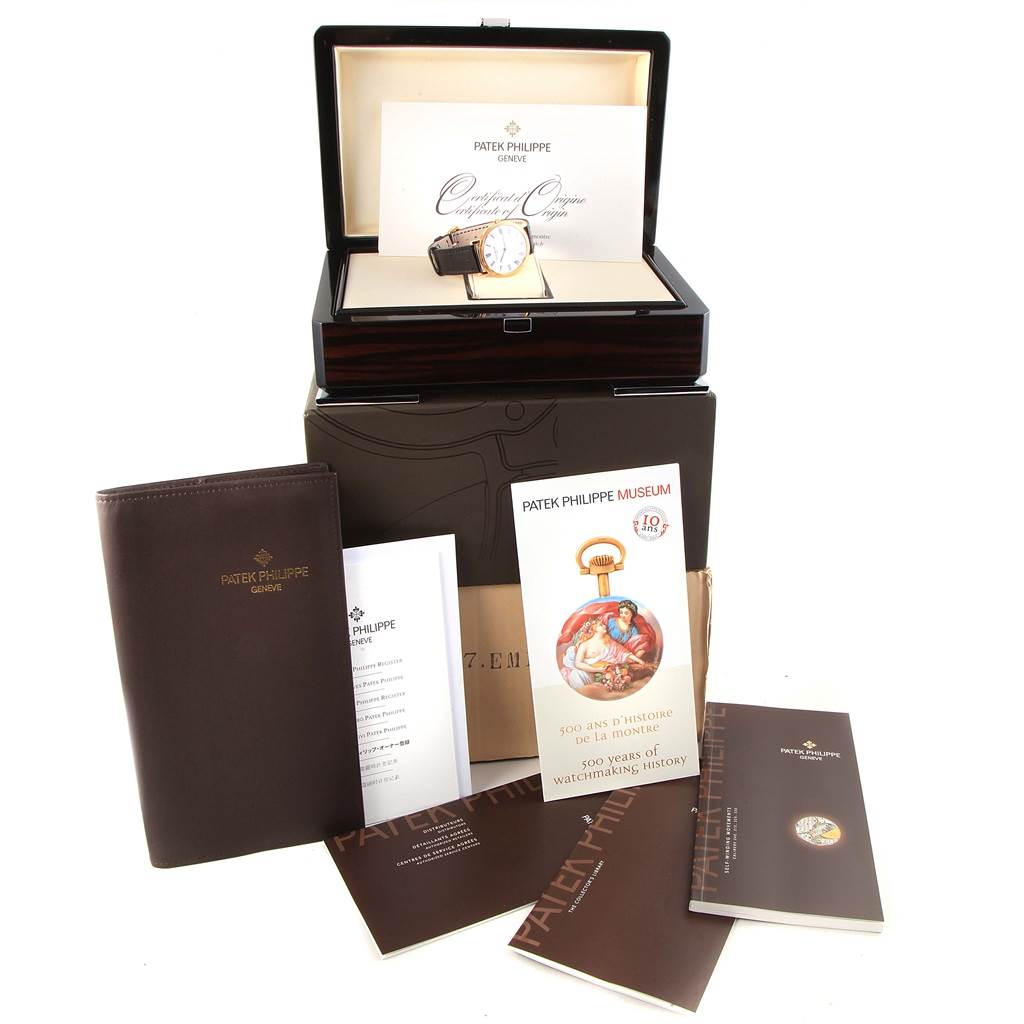 The image shows a Patek Philippe Calatrava 5120J Men's Yellow Gold White Dial 5120J Men's Yellow Gold White Dial watch in its box, with accompanying booklets, certificate, and additional packaging materials.