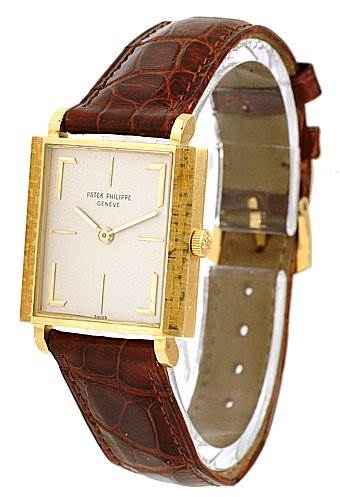 The image shows a Vintage model by Patek Philippe from a three-quarter angle, highlighting the square dial, gold casing, and brown leather strap.