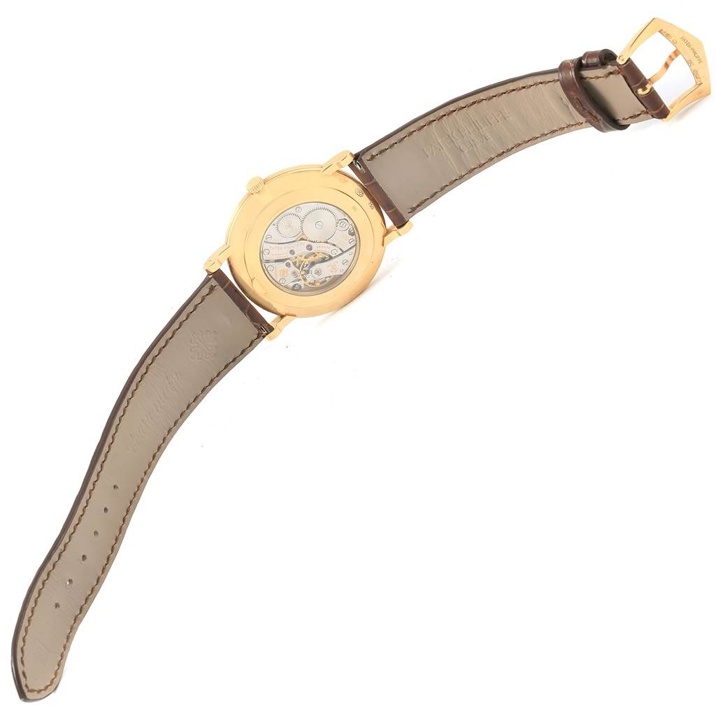 The image shows the back view of a Patek Philippe Calatrava 5119J Men's Yellow Gold White Dial 5119J Men's Yellow Gold White Dial watch, displaying its intricate mechanical movement and brown leather strap.