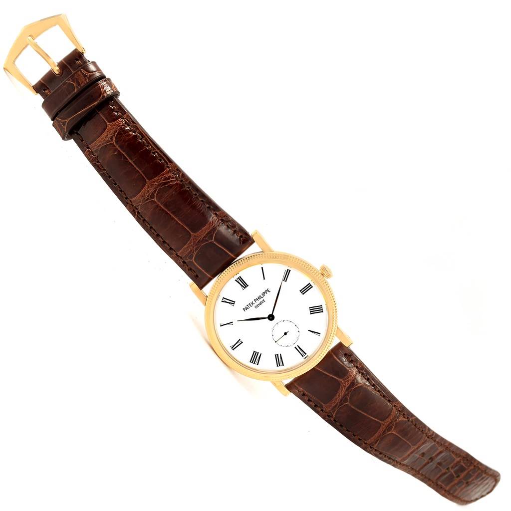 The image shows a Patek Philippe Calatrava 5119J Men's Yellow Gold White Dial 5119J Men's Yellow Gold White Dial watch from a top-down angle, featuring its brown leather strap and a white dial with Roman numerals.