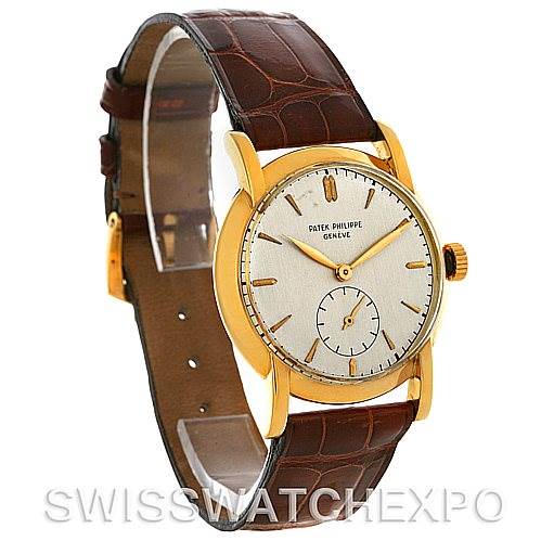 The image shows a vintage Patek Philippe watch at a three-quarter angle, highlighting its gold case, white dial, and brown leather strap.