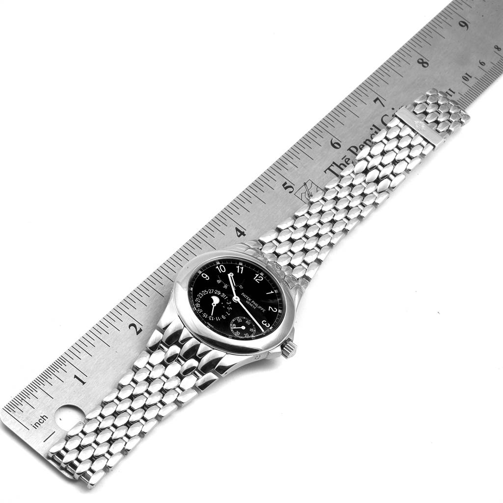 The Neptune model by Patek Philippe is shown from a top-down angle alongside a ruler, displaying its face and metal bracelet.