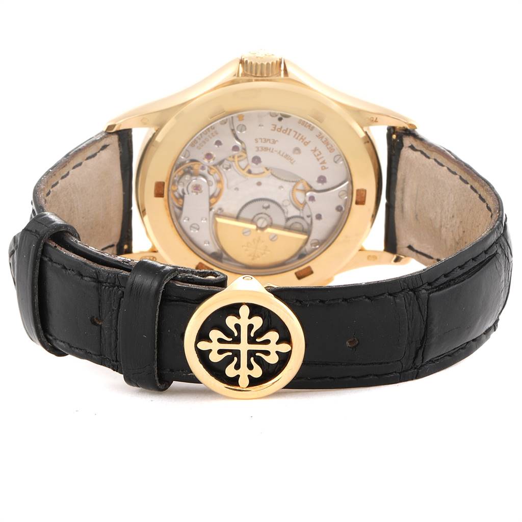 The image shows the back view of the Patek Philippe Complications 5110J Men's Yellow Gold Silver Dial 5110J Men's Yellow Gold Silver Dial watch, highlighting the movement and leather strap with logo.