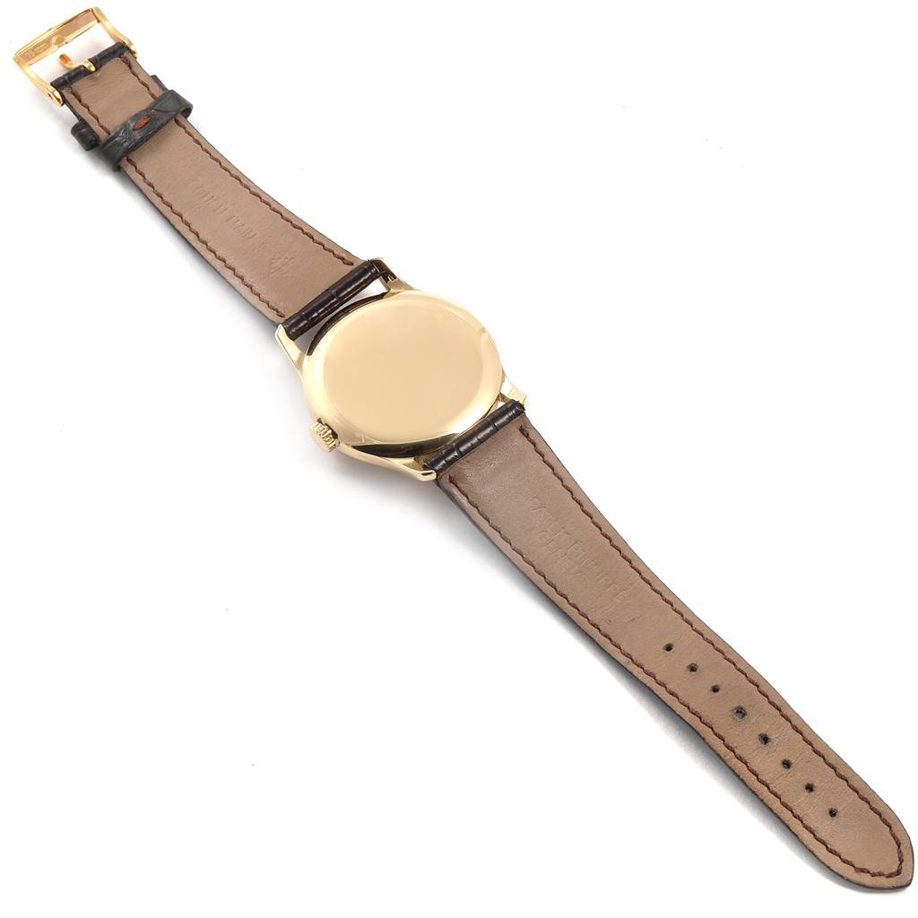 The Vintage Patek Philippe watch is shown from the back, displaying its golden case and brown leather strap.