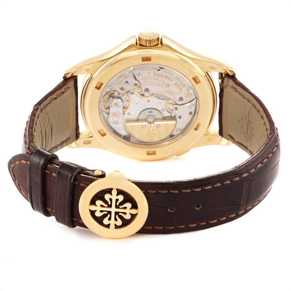 The image shows the backside of the Patek Philippe Complications 5130J Men's Yellow Gold Silver Dial 5130J Men's Yellow Gold Silver Dial watch, highlighting its movement and leather strap with a branded clasp.