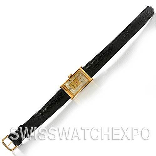 This image shows a vintage Patek Philippe watch with a rectangular gold case and black leather strap, viewed from a top-down angle.