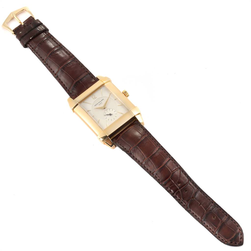 The image shows a top-down view of the Patek Philippe Gondolo 51111J Men's Yellow Gold Silver Dial 51111J Men's Yellow Gold Silver Dial watch, highlighting its rectangular face, gold case, and brown leather strap.