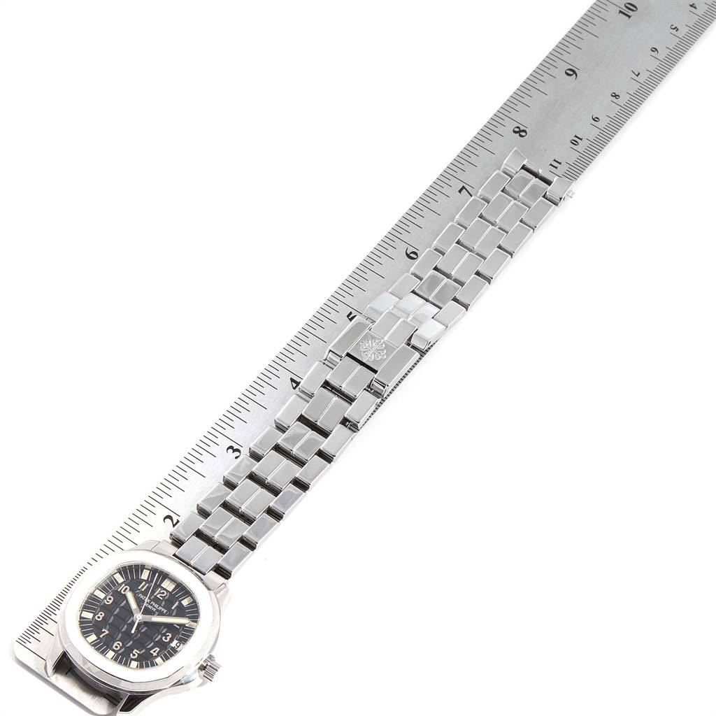 The image shows an angled view of the Patek Philippe Aquanaut 5065/1A-010 Men's Stainless Steel Black Dial 5065/1A-010 Men's Stainless Steel Black Dial watch with a focus on its bracelet laying against a ruler for scale.