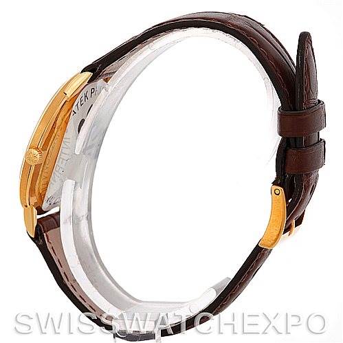 The image shows the side profile of a vintage Patek Philippe watch, highlighting the gold case, crown, and brown leather strap.