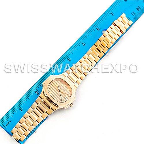 This image shows a Patek Philippe Nautilus 3900/1J Men's Yellow Gold Champagne Dial 3900/1J Men's Yellow Gold Champagne Dial watch laid flat with a blue ruler beside it for scale.